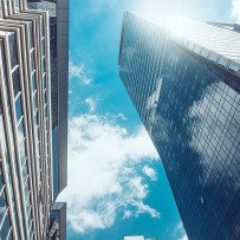 looking-up-between-commercial-skyscrapers-to-blue-sky-with-clouds-gettyimages-1266657702-1300w-867h